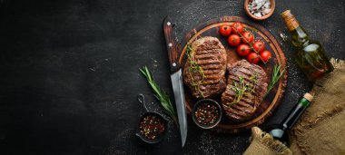 Izgara ribeye sığır eti biftek, otlar ve baharatlar karanlık bir masada. Üst te. Metniniz için boş alan.
