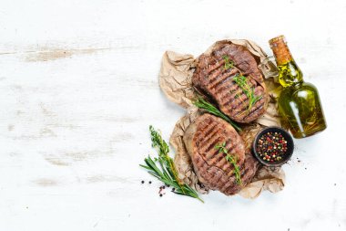 Izgara ribeye sığır eti biftek, otlar ve baharatlar beyaz ahşap arka plan üzerinde. Üst te. Metniniz için boş alan.