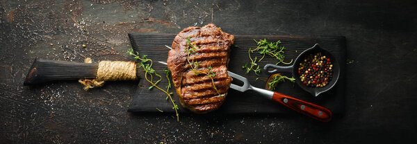 Grilled ribeye beef steak, herbs and spices on a dark table. Top view. Free space for your text.