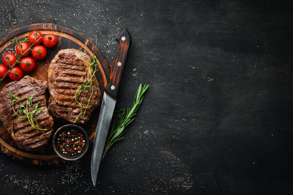Grilled ribeye beef steak, herbs and spices on a dark table. Top view. Free space for your text.