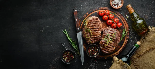 Izgara ribeye sığır eti biftek, otlar ve baharatlar karanlık bir masada. Üst te. Metniniz için boş alan.