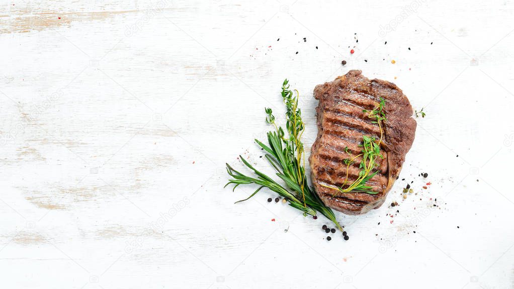 Grilled ribeye beef steak, herbs and spices on a white wooden background. Top view. Free space for your text.