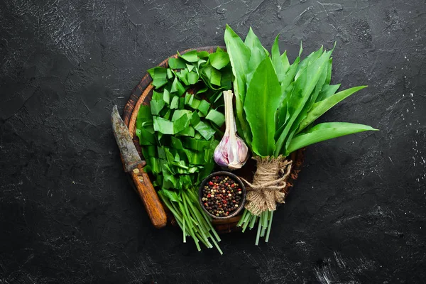 Fresh wild garlic leaves on black background. Wild leek. Top view. Free space for your text.