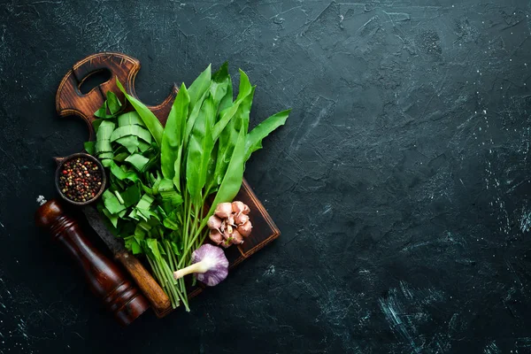 Fresh wild garlic leaves on black background. Wild leek. Top view. Free space for your text.