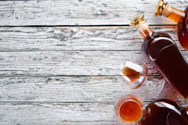 Beyaz ahşap arka plan üzerinde bir şişe konyak ve gözlük. Brendi, ne kadar. Üst te. Metniniz için boş alan.