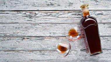 Beyaz ahşap arka plan üzerinde bir şişe konyak ve gözlük. Brendi, ne kadar. Üst te. Metniniz için boş alan.