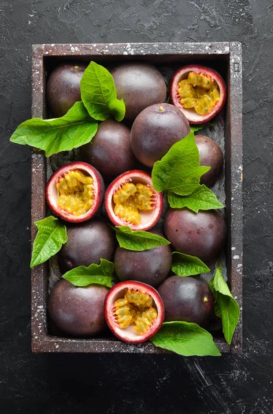 Passion fruits with leaves on a black background. Tropical Fruits. Top view. Free space for text.