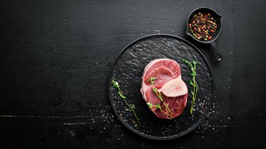 Siyah bir arka plan üzerinde baharat ve otlar ile Osso Buco yapmak için Ham taze çapraz kesilmiş dana sapı. Üst te. Metniniz için boş alan.