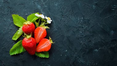 Siyah taş arka plan üzerinde yaprakları ile taze çilek. Çilek Üst görünüm. Metniniz için boş alan.