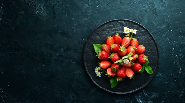 Siyah taş zemin üzerinde bir tabakta taze çilek. Çilek Üst görünüm. Metniniz için boş alan.