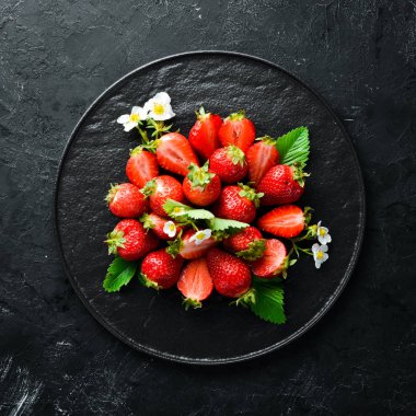 Siyah taş zemin üzerinde bir tabakta taze çilek. Çilek Üst görünüm. Metniniz için boş alan.