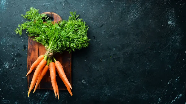 Fresh carrots on a black stone background. Top view. Free space for your text.