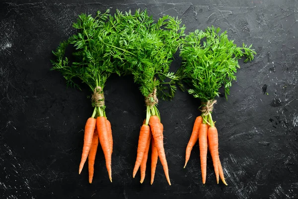 Fresh carrots on a black stone background. Top view. Free space for your text.