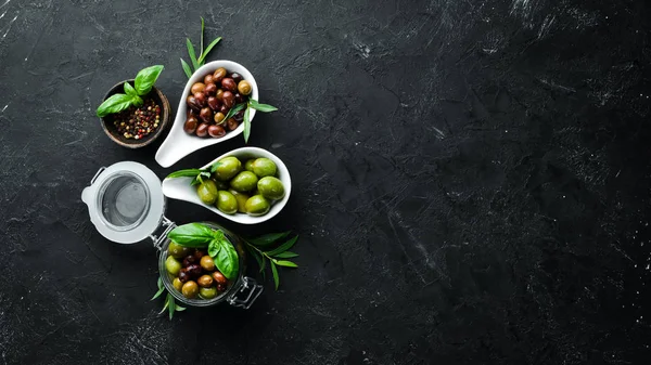 Olives A set of colored olives on a black stone background. Top view. Free space for your text.