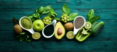 Sağlıklı Yeşil gıda. Meyve ve sebzeler - avokado, limon, soğan, elma, kivi, spirulina. Mavi ahşap bir arka plan üzerinde. Üst te. Metniniz için boş alan.