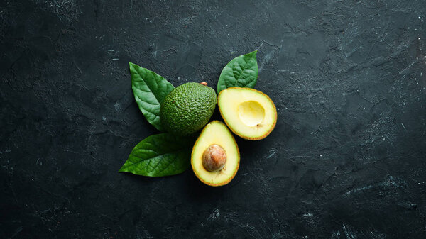 Fresh avocado with leaves on a black background. Top view. Free space for your text.