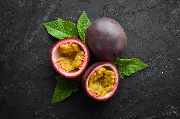 Passion fruits with leaves on a black background. Tropical Fruits. Top view. Free space for text.