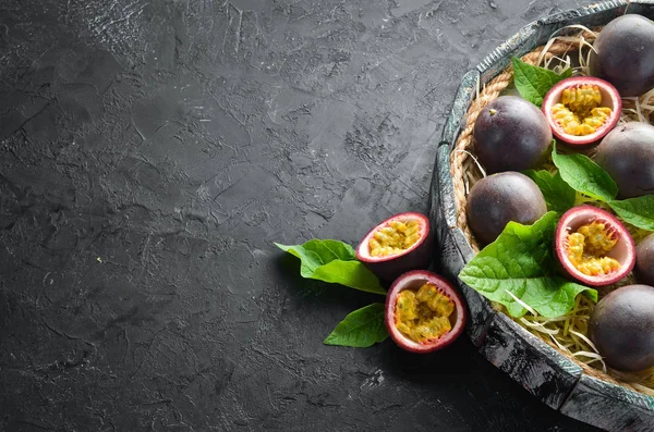 Passion fruits with leaves on a black background. Tropical Fruits. Top view. Free space for text.