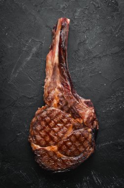 Izgara kovboy et biftek, otlar ve baharatlar siyah taş arka plan üzerinde. Barbekü. Üst te. Metin için boş alan.
