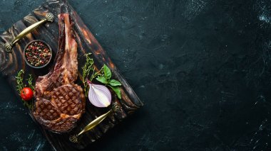 Izgara kovboy et biftek, otlar ve baharatlar siyah taş arka plan üzerinde. Barbekü. Üst te. Metin için boş alan.