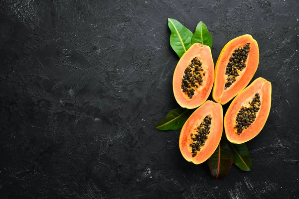 Fresh papaya on a black stone background. Tropical Fruits. Top view. Free space for text.
