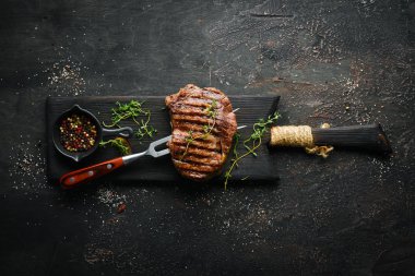 Izgara ribeye sığır eti biftek, otlar ve baharatlar karanlık bir masada. Üst te. Metniniz için boş alan.