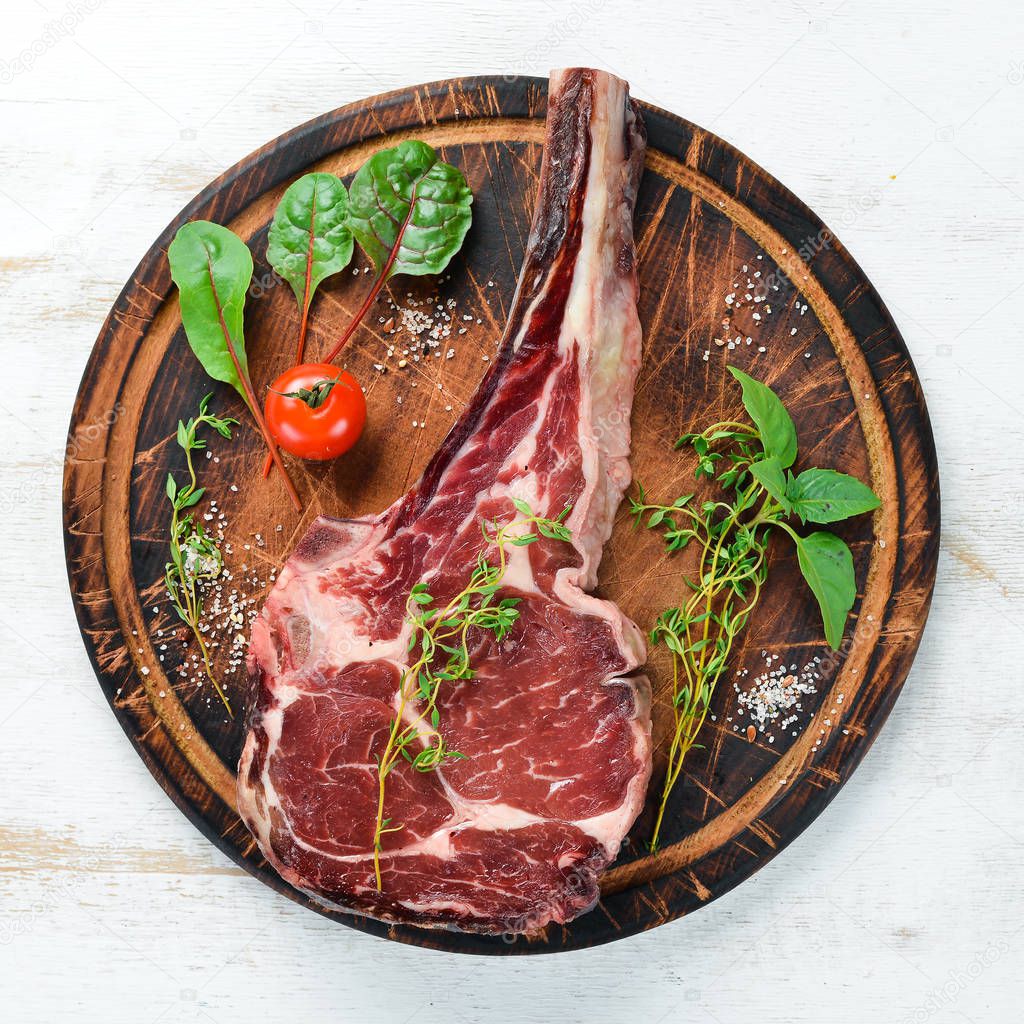 Raw cowboy steak and spices on a white wooden background. BBQ Top view. Free space for text.