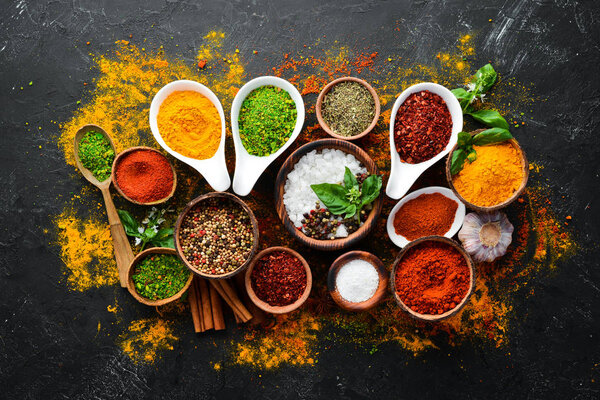 Colorful herbs and spices for cooking. Indian spices. On a black stone background. Top view.