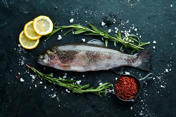 Raw fish trout with vegetables on a black stone background. Top view. Free space for your text.