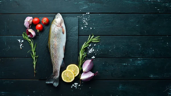 Raw fish with vegetables on a black wooden background. Fish trout. Top view. Free space for your text.
