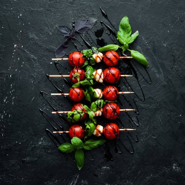 Kiraz domates, mozzarella ve fesleğen. Siyah taş bir arka plan üzerinde. İtalyan mutfağı. Üst te. Metniniz için boş alan.