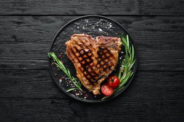 Biberiye ve baharatlar ile ızgara T-kemik biftek. Eski bir arka planda. Üst te. Ücretsiz kopyalama alanı.