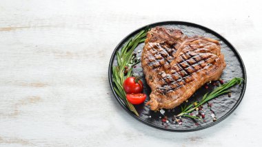 Biberiye ve baharatlar ile ızgara T-kemik biftek. Eski bir arka planda. Üst te. Ücretsiz kopyalama alanı.