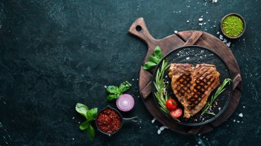 Biberiye ve baharatlar ile ızgara T-kemik biftek. Eski bir arka planda. Üst te. Ücretsiz kopyalama alanı.