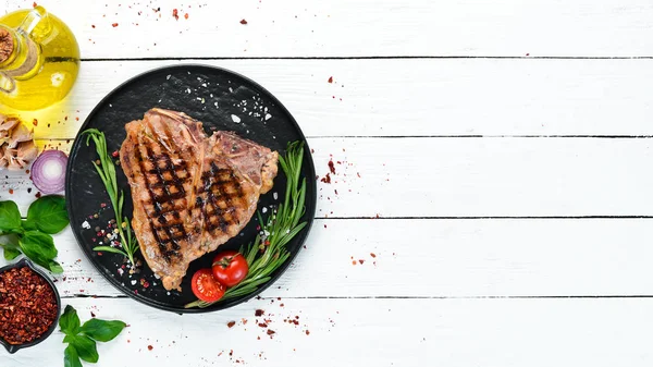 Biberiye ve baharatlar ile ızgara T-kemik biftek. Eski bir arka planda. Üst te. Ücretsiz kopyalama alanı.