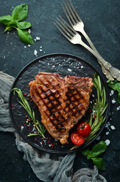 Biberiye ve baharatlar ile ızgara T-kemik biftek. Eski bir arka planda. Üst te. Ücretsiz kopyalama alanı.
