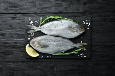 Limon, tuz ve biberiye ile çiğ deniz balığı. Siyah bir arka plan üzerinde. Üst te. Ücretsiz kopyalama alanı.