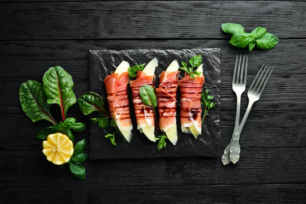 Prosciutto with melon on a stone plate. Traditional Italian appetizer. Top view. Free copy space.