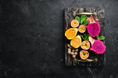 Tropikal meyve - siyah bir arka plan üzerinde tutku meyve, ananas, ejderha meyve, kivi ve kaktüs. Üst te. Metin için boş alan.