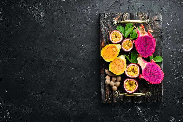 Tropikal meyve - siyah bir arka plan üzerinde tutku meyve, ananas, ejderha meyve, kivi ve kaktüs. Üst te. Metin için boş alan.