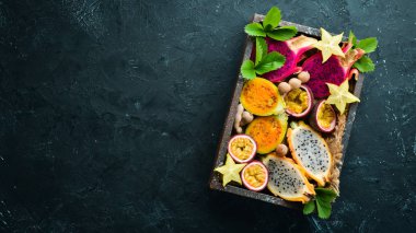 Tropikal meyve - siyah bir arka plan üzerinde tutku meyve, ananas, ejderha meyve, kivi ve kaktüs. Üst te. Metin için boş alan.