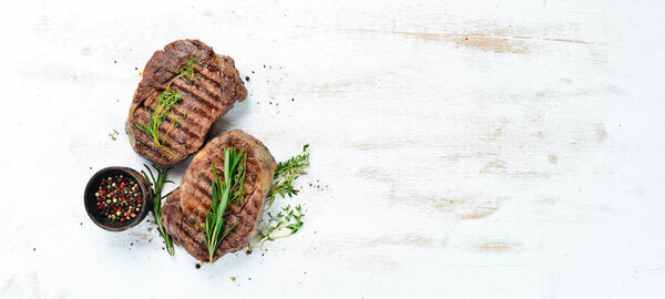 Grilled ribeye beef steak, herbs and spices on a white wooden background. Top view. Free space for your text.