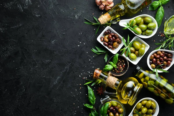 Olive oil, olives and spices on a black stone background. Top view. Free space for your text.