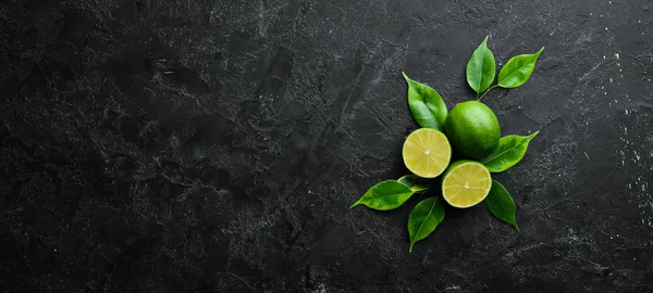 Fresh green limes with leaves. Citrus fruits. On a black stone background. Top view. Free space for your text.