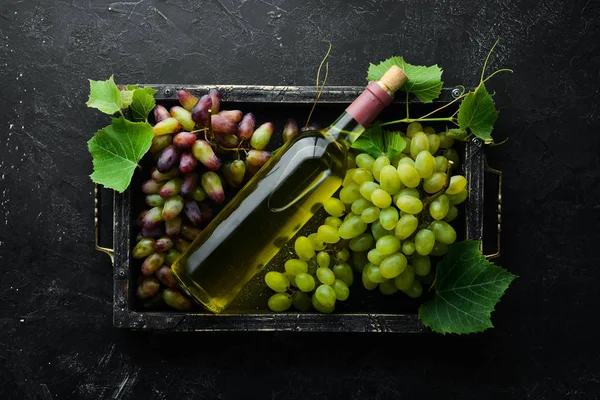 Bottle of white wine and fresh grapes on a black stone table. Top view. Free space for your text.