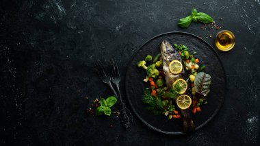 Siyah tabakta sebzeli ve limonlu fırında balık. Üst Manzara. Boş kopyalama alanı.