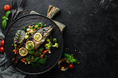 Siyah tabakta sebzeli ve limonlu fırında balık. Üst Manzara. Boş kopyalama alanı.