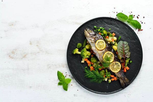 Siyah tabakta sebzeli ve limonlu fırında balık. Üst Manzara. Boş kopyalama alanı.