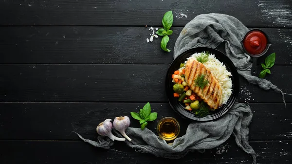 Baked chicken fillet with rice and vegetables on a black plate. Top view. Free copy space.