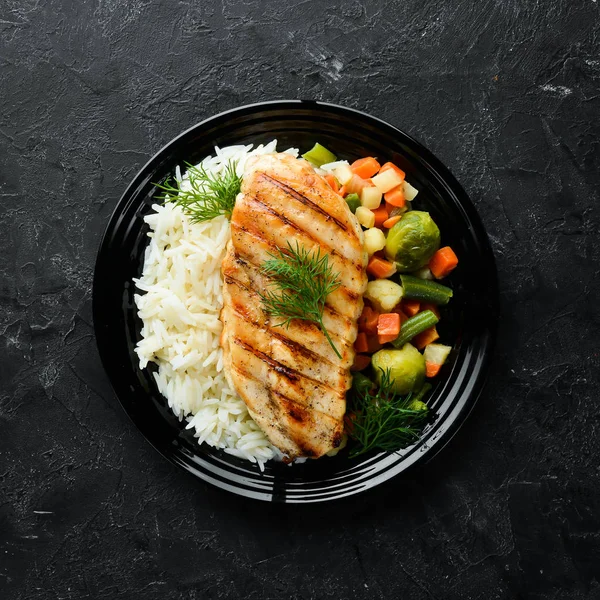 Baked chicken fillet with rice and vegetables on a black plate. Top view. Free copy space.